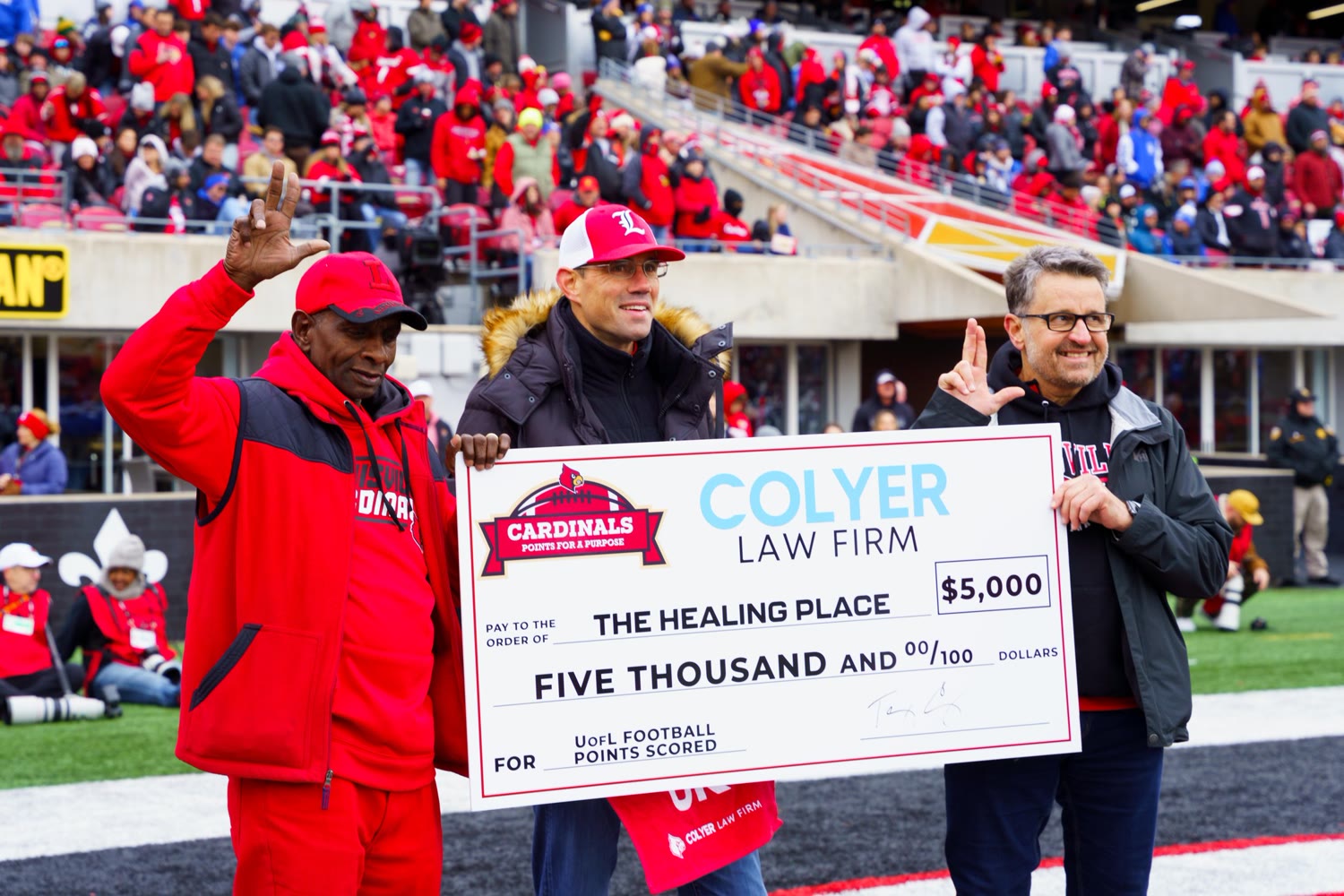 Colyer Law presents a $5,000 check to The Healing Place on the field at a University of Louisville game.